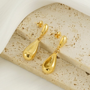 Elegante goldene Tropfenohrringe aus poliertem Titanstahl auf weißem Travertin-Stein