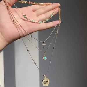Detail of four-layered gold necklace with green beads, cross, and engraved coin pendant