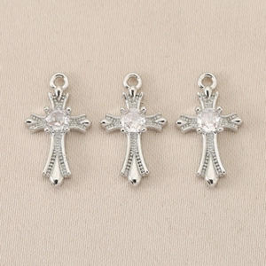 Detailed view of three silver plated cross pendants with inlaid zircon stones on beige fabric
