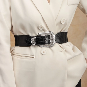 Detail of black faux crocodile belt with rhinestone buckle over a beige blazer