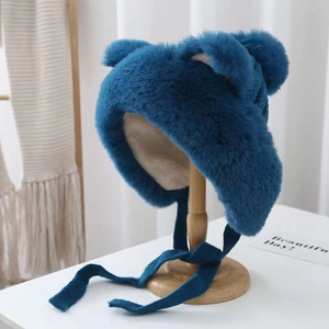 Close-up of peacock blue plush earflap hat with bear ears on a wooden stand