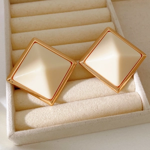 Macro detail of geometric square stud earrings in cream resin with gold-tone metal edges