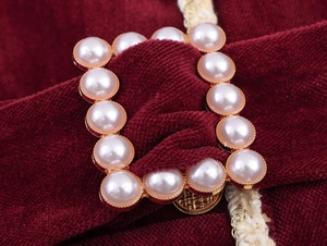 Detailed view of elegant square gold button with pearl on burgundy chenille fabric