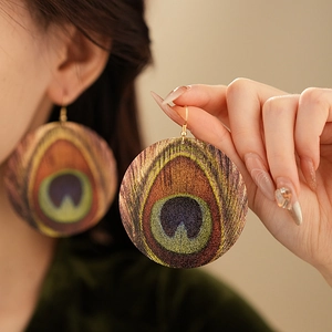 Detailed view of large round peacock feather pattern earrings with gold hooks