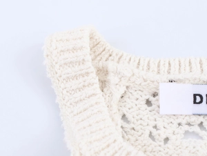 Detailed view of the ribbed neckline and intricate hollow crochet pattern on a cream knit dress