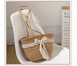 Detail view of straw woven handbag featuring a delicate white lace bow and sturdy handles