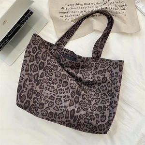 Top view of a large leopard print tote bag placed on a bed with a laptop and accessories