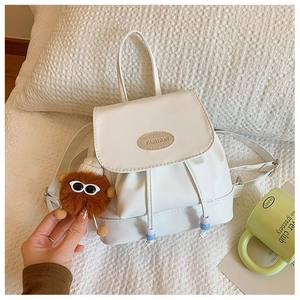 Detail of white drawstring backpack with fashion label and brown plush bear charm