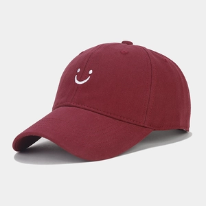 Detailed close-up of white smiling face embroidery on a burgundy cotton baseball cap