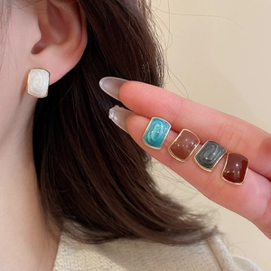 Close-up of colorful resin square stud earrings with gold metal edges on a hand