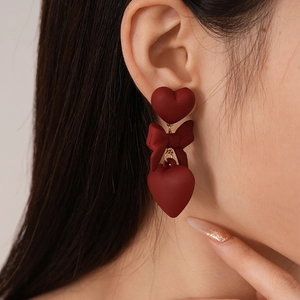 Detail of matte dark red bow and heart drop earrings on model for an elegant look