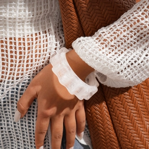 Macro detail of white wavy acrylic bracelet with ice-crack texture on a woven background