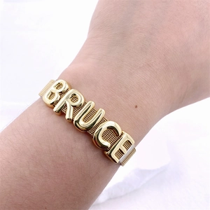 Detailed macro view of a gold mesh band bracelet with BRUCE lettering on white fabric