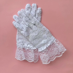 Close-up of white floral lace gloves with ruffled cuffs on pink background