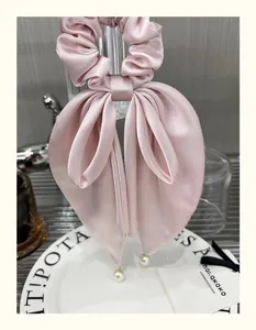 Close-up of pink satin bow hair tie featuring elegant hanging white pearl charms