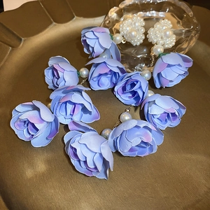 Detailed close-up of long purple fabric flower earrings with white pearls on a vintage tray