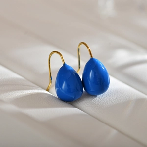 Detailed close-up of Klein blue water drop earrings with elegant gold hooks on white leather