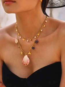 Detail of layered gold necklace with shell, turtle and fishtail charms on a model