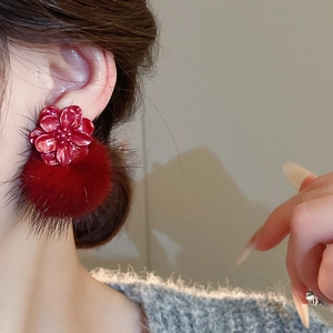 Close-up of red resin flower and faux fur pom pom earrings worn by a female model
