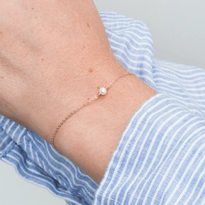 Detail eines Roségold-Perlenarmbands am Handgelenk mit elegantem minimalistischem Design