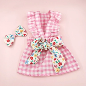 Detailed view of pink plaid pet dress with floral bow accessory on soft background