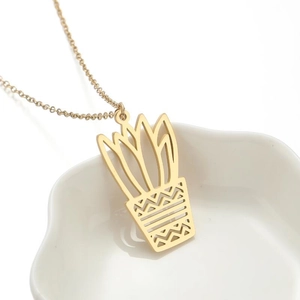 Elegant gold cactus pendant necklace on white ceramic plate, minimalist jewelry style