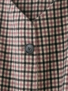 Close-up of elegant plaid fabric texture and a black four-hole button on a long coat
