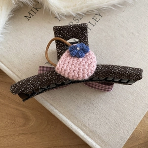 Close-up of a tweed hair claw clip featuring a knitted bag charm on a book background