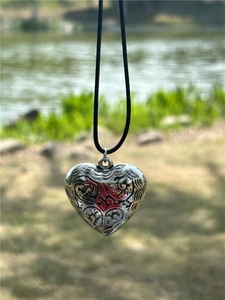 Detailed macro view of an engraved silver heart pendant on a black cord necklace