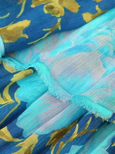 Detailed close-up of blue floral chiffon fabric with fringe edges and turquoise panels