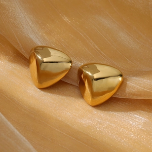 Macro shot of polished gold triangular pyramid stud earrings on champagne silk fabric