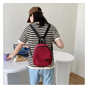 Close-up of a vintage red corduroy mini backpack worn by a model in a minimal indoor setting
