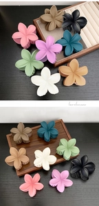 Close-up of matte plumeria hair claws in various Morandi colors on a luxury wooden tray