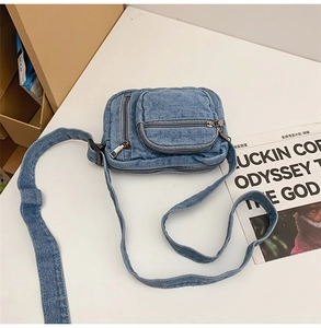 Top-down view of a blue denim crossbody bag with multiple zipper pockets on a white desk