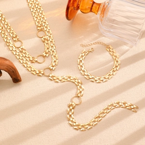 Detail of matte gold multi-layer tank chain with large ring pendant on a textured background