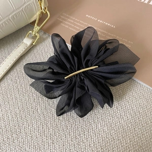 Détail d'une élégante pince à cheveux fleur en organza noir avec barre en métal doré