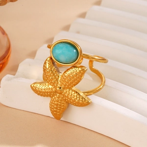 Golden starfish ring with blue oval gemstone on white minimalist platform
