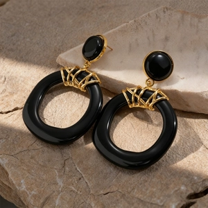 Detail of black resin hoop earrings with golden metal wrapping on a stone background