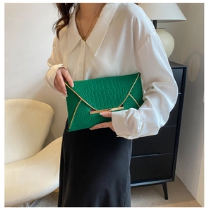 Détail de la pochette enveloppe verte à texture crocodile et bordure dorée