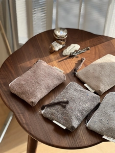 Detail view of four tweed herringbone mini pouches with zippers on a wooden table