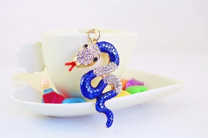 Close-up of blue enamel snake keychain with sparkling rhinestones on a coffee cup