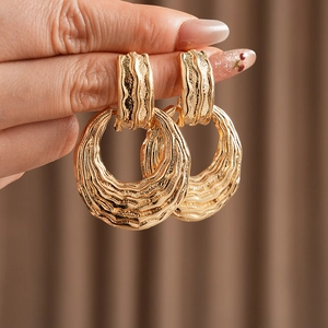 Macro shot of gold-plated textured round earrings held by hand showing intricate details