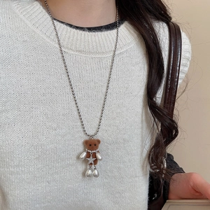 Detail of brown flocked bear necklace with pearl and silver star on white knit sweater