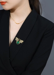Detailed close-up of a vintage bee brooch with green gem pinned on a black blazer