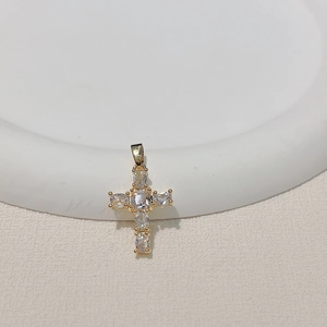 Detailed close-up of gold plated cross pendant with clear zircon stones on a white plate