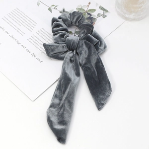 Detailed view of grey velvet scrunchie with bow and vertical stripe texture on magazine