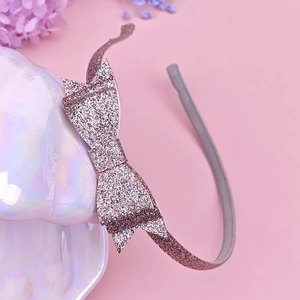 Detail view of a rose gold sequined bow headband placed on a decorative shell