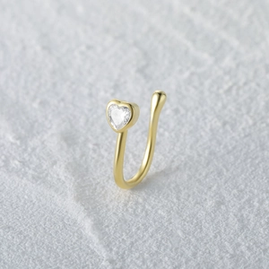 Close-up of heart-shaped gold nose cuff with a sparkling zircon on a white stone surface
