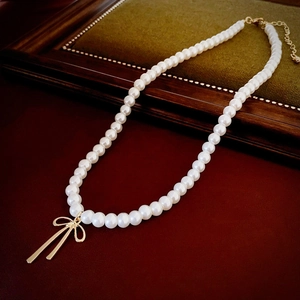 Macro shot of faux pearl choker with gold bow pendant and adjustable lobster clasp closure