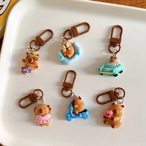 Set of six cute cartoon capybara keychains in various poses on a white ceramic tray